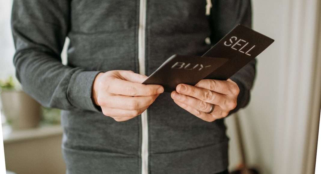 Man looking at two cards that say buy or sell