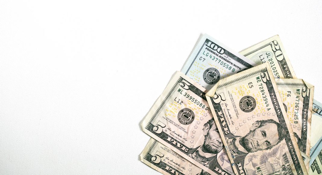 A small pile of USD / American Dollar Bills fanned out nicely in the corner of a simple white background.